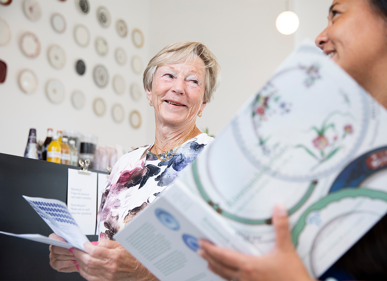 Äldre kvinna ler mot annan kvinna i cafét på Rörstrand Museum.