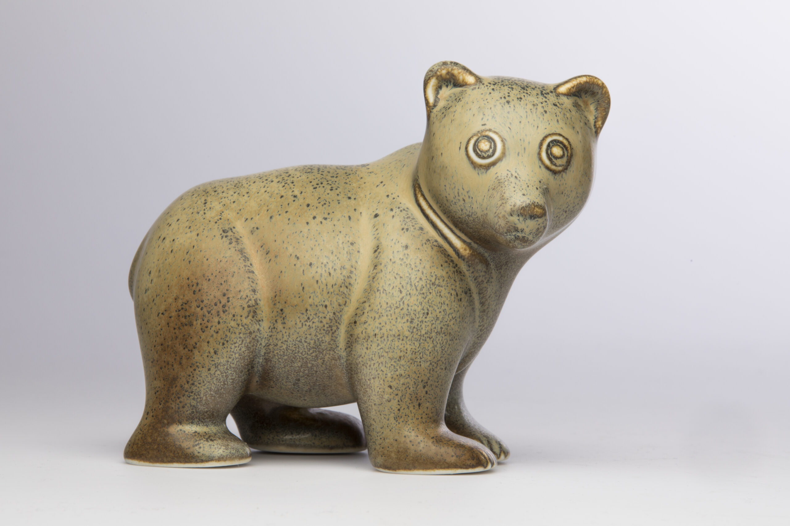 Guldrig björn i keramik mot ljus bakgrund.