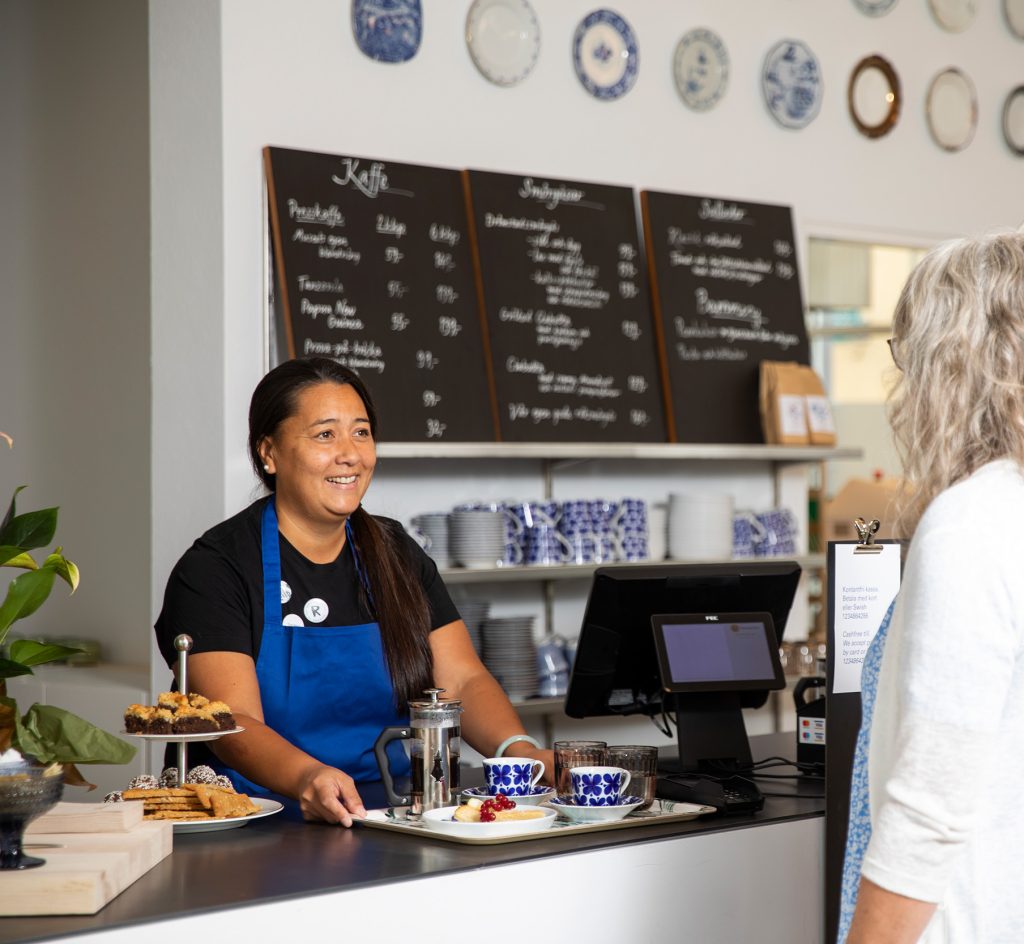 Personal på Rörstrand museums kafé som serverar en bricka fylld med fika för en besökare.
